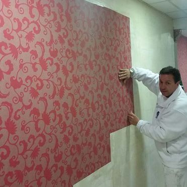 Hombre instalando papel tapiz floral rojo en una pared beige.
