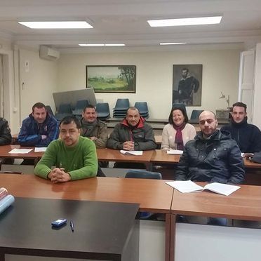 Personas sentadas en escritorios en un aula, mirando a la cámara.