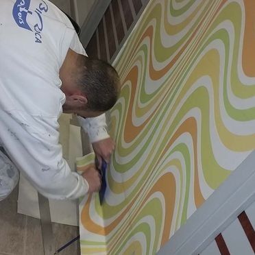 Persona instalando papel tapiz ondulado y colorido en una pared.