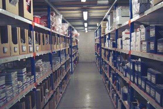 Pasillo de almacén con filas de estantes apilados con cajas y contenedores.
