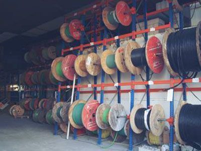 Estantes que contienen numerosos carretes de cables eléctricos de colores en un almacén.
