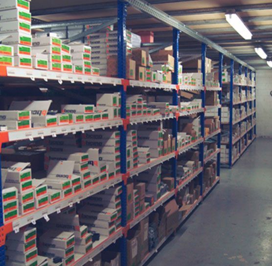 Interior de almacén con filas de estanterías metálicas repletas de cajas de distintos tamaños, principalmente blancas y marrones.