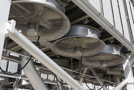 Ventiladores industriales de gran tamaño montados debajo de una estructura metálica, probablemente para refrigeración o ventilación en una fábrica o planta.