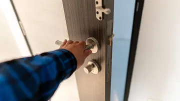 Una mano se extiende para girar el pomo plateado de una puerta de madera oscura.
