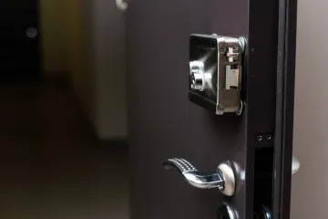 Primer plano de una puerta negra parcialmente abierta con manija y pestillo plateados.