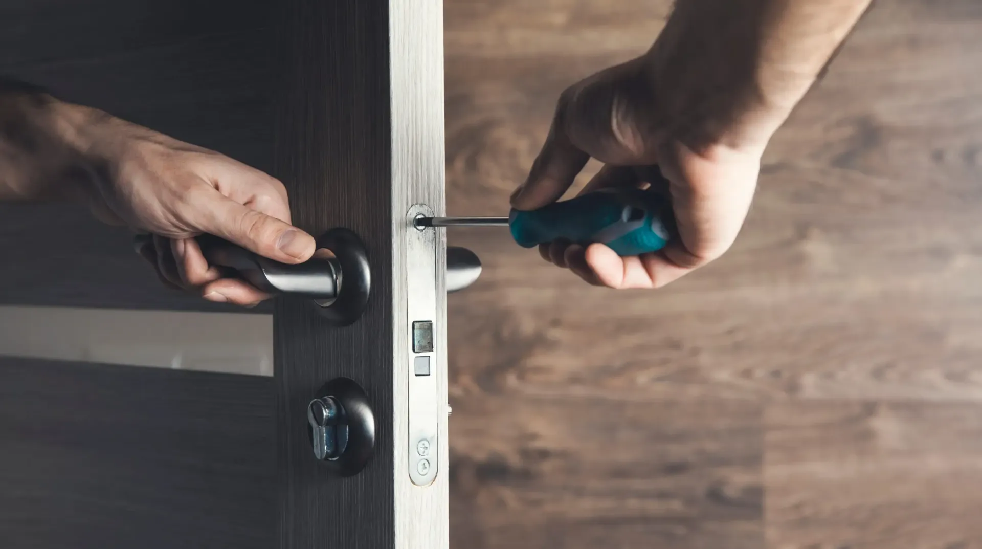 Manos usando un destornillador y una manija de puerta para instalar una cerradura en una puerta de madera.