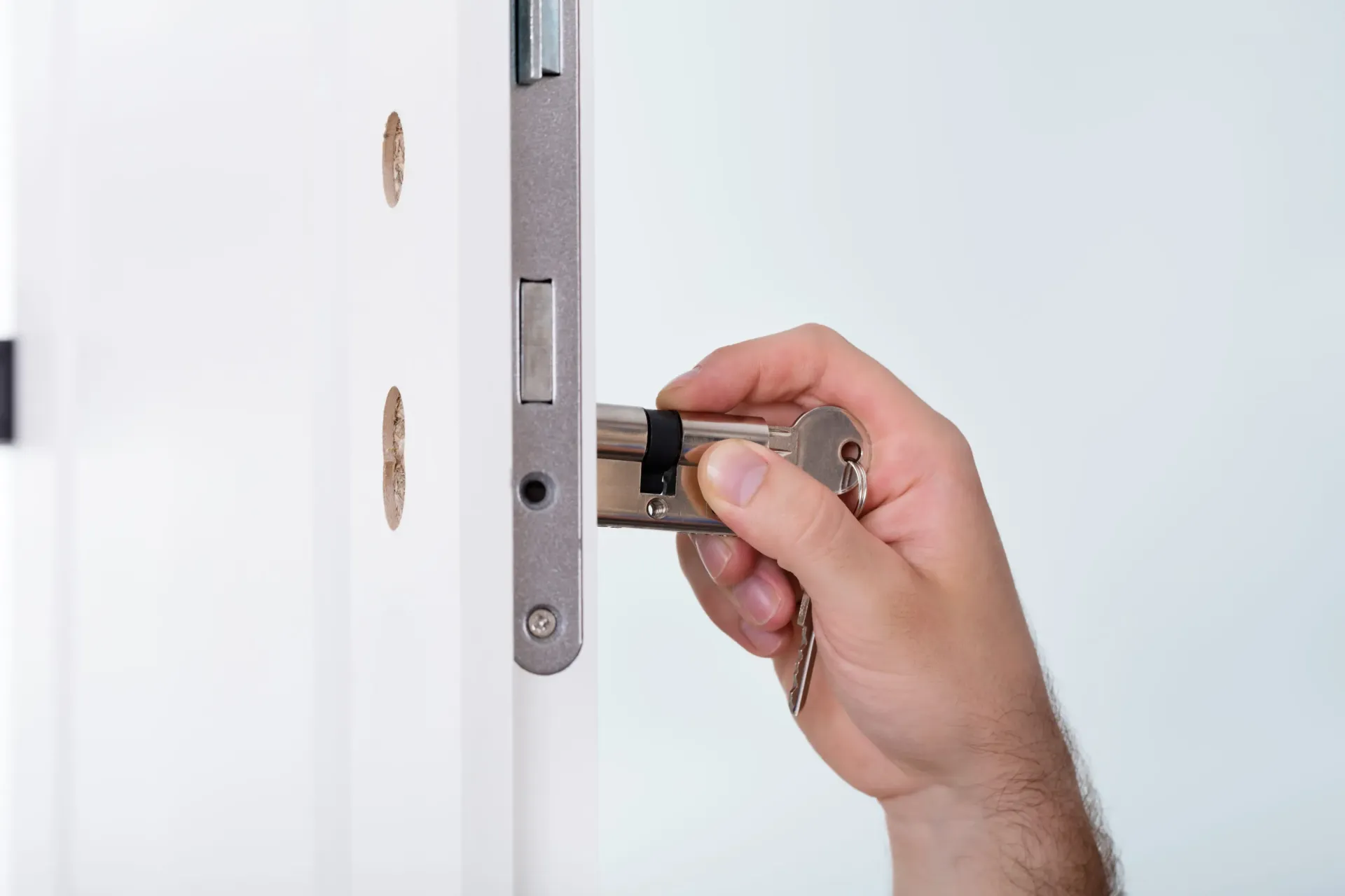 Una mano inserta una llave en la cerradura de una puerta blanca.