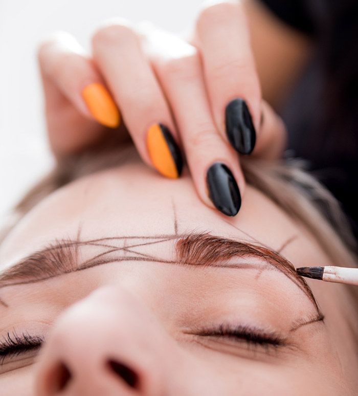 Una mujer con uñas negras se está pintando las cejas.