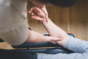 Manos manipulando suavemente un antebrazo en el regazo de una persona, probablemente proporcionando terapia o tratamiento médico.