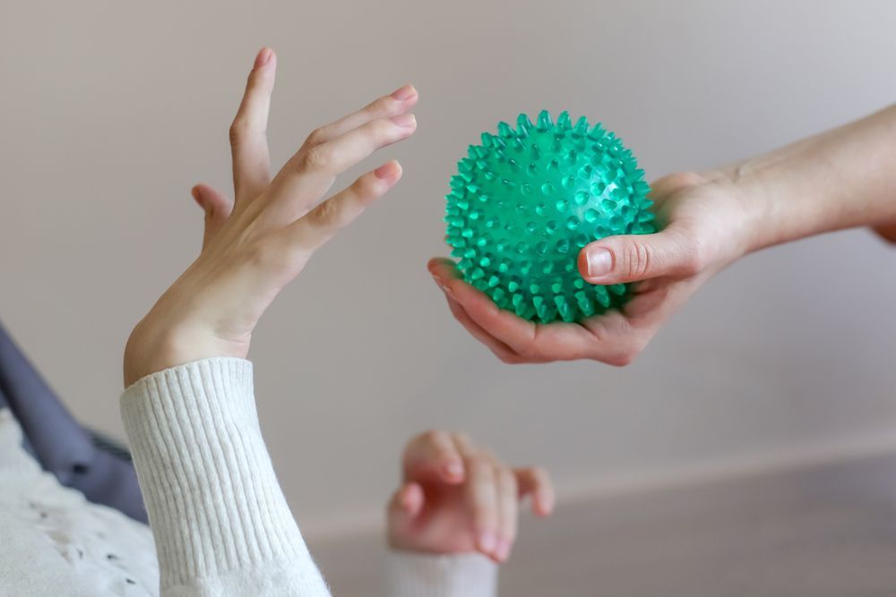 Persona que ofrece una pelota verde con púas a otra persona con la mano levantada; en el interior.