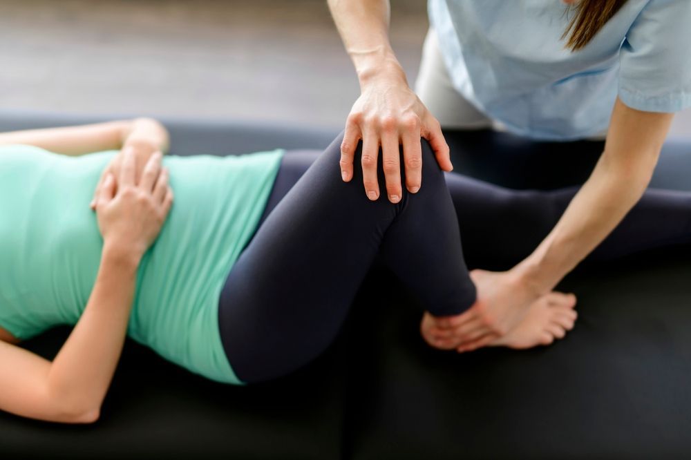 Persona que recibe fisioterapia, terapeuta manipulando rodilla y tobillo.