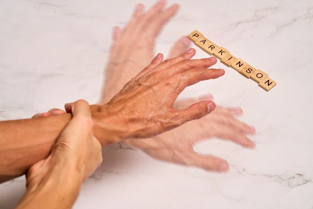 Mano temblorosa debido al Parkinson, otra mano sosteniéndola, con las letras