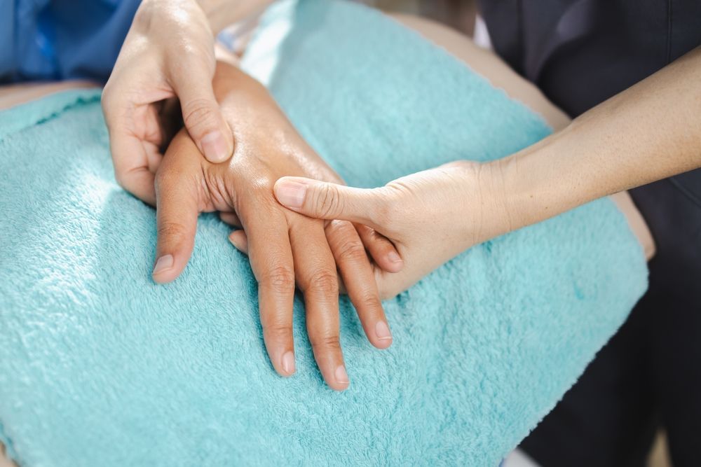 Manos recibiendo un masaje de manos sobre una toalla azul claro.