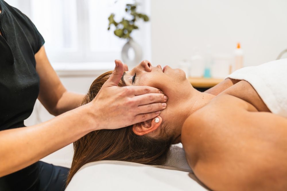 Mujer recibiendo un masaje facial en un spa; las manos del terapeuta en su rostro.