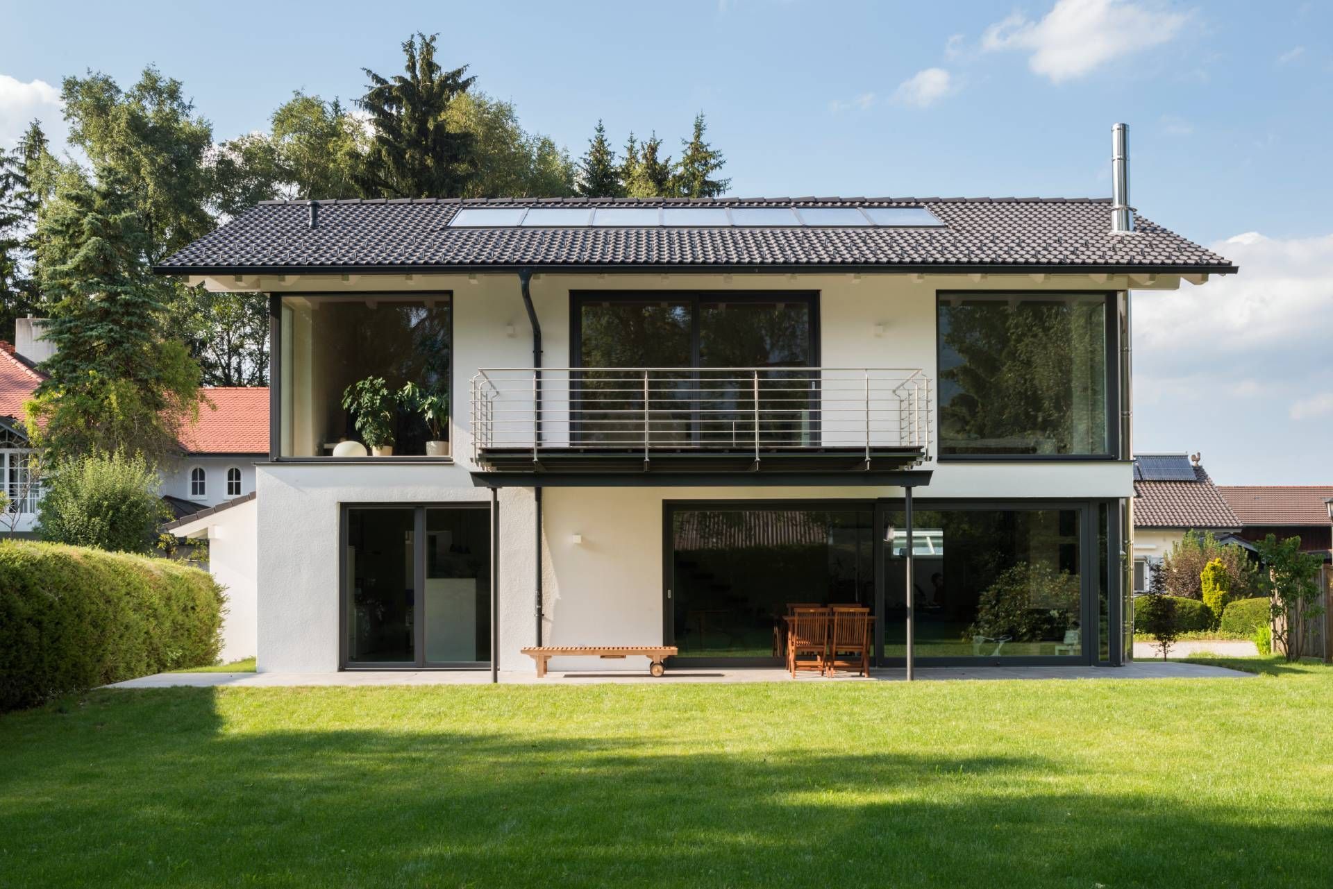 Weißes Haus mit dunklem Dach und großen Fenstern und einer Wiese davor