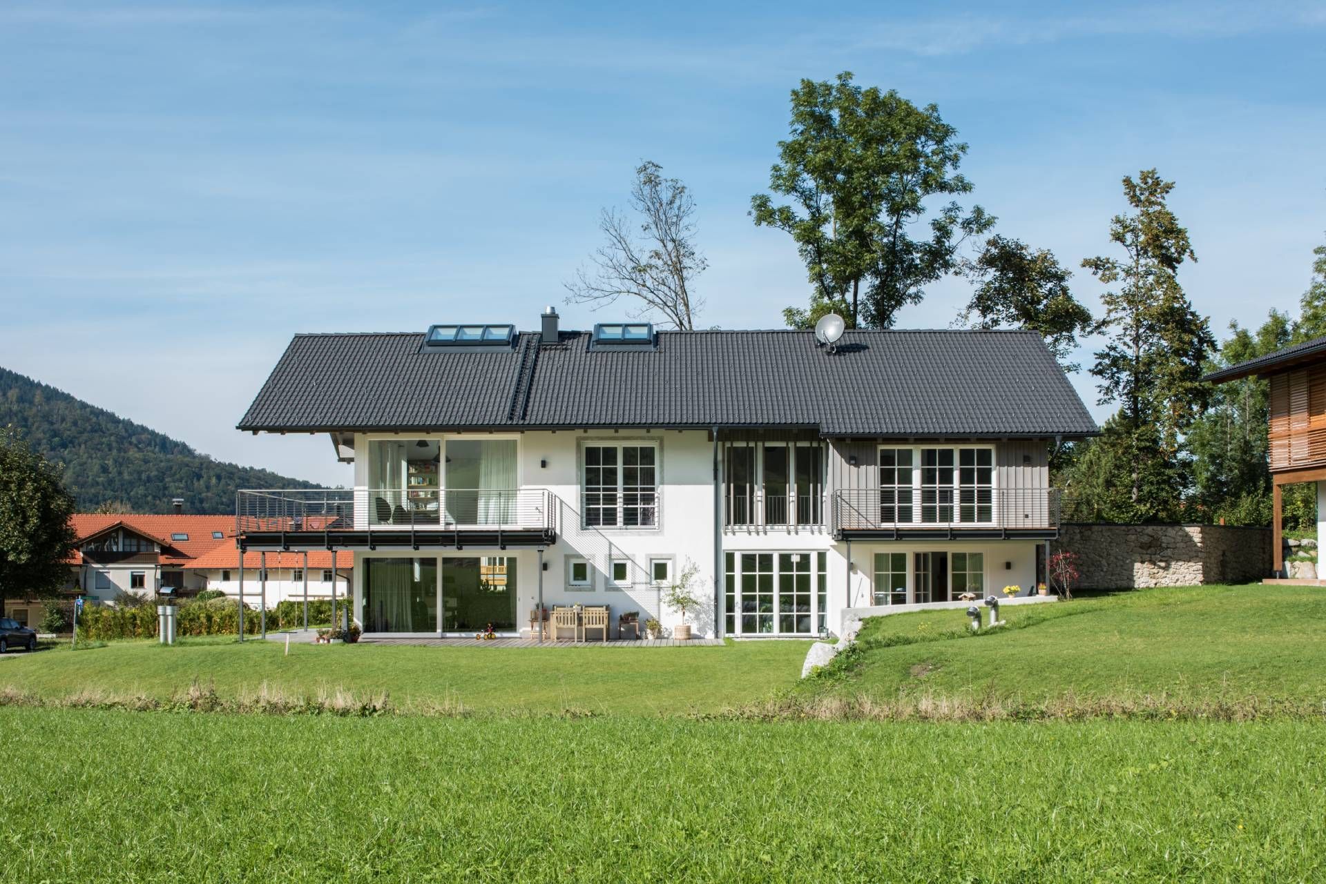 Weißes Haus mit dunklem Dach und großen Fenstern und einer Wiese davor