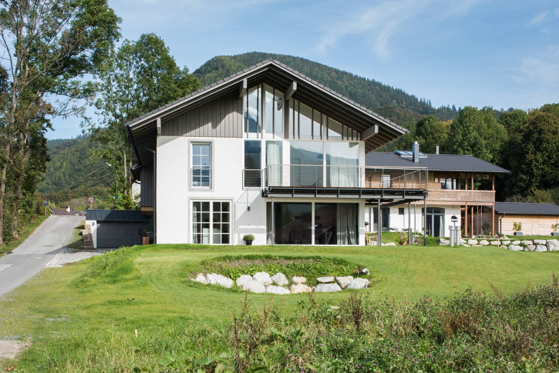 Weißes Haus mit dunklem Dach und großen Fenstern und einer Wiese davor