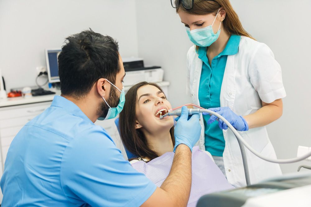 Una mujer está sentada en una silla dental mientras un dentista le examina los dientes.