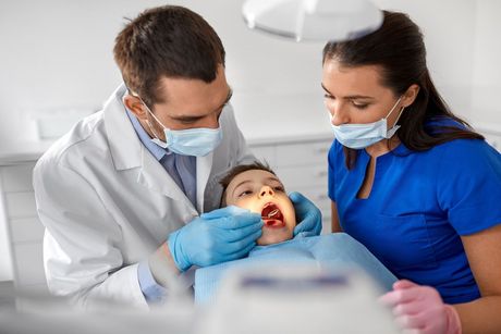Un dentista y una enfermera están examinando los dientes de un niño en un consultorio dental.