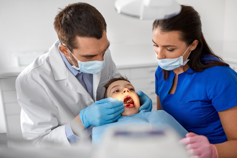 Un dentista y una enfermera están examinando los dientes de un niño en un consultorio dental.