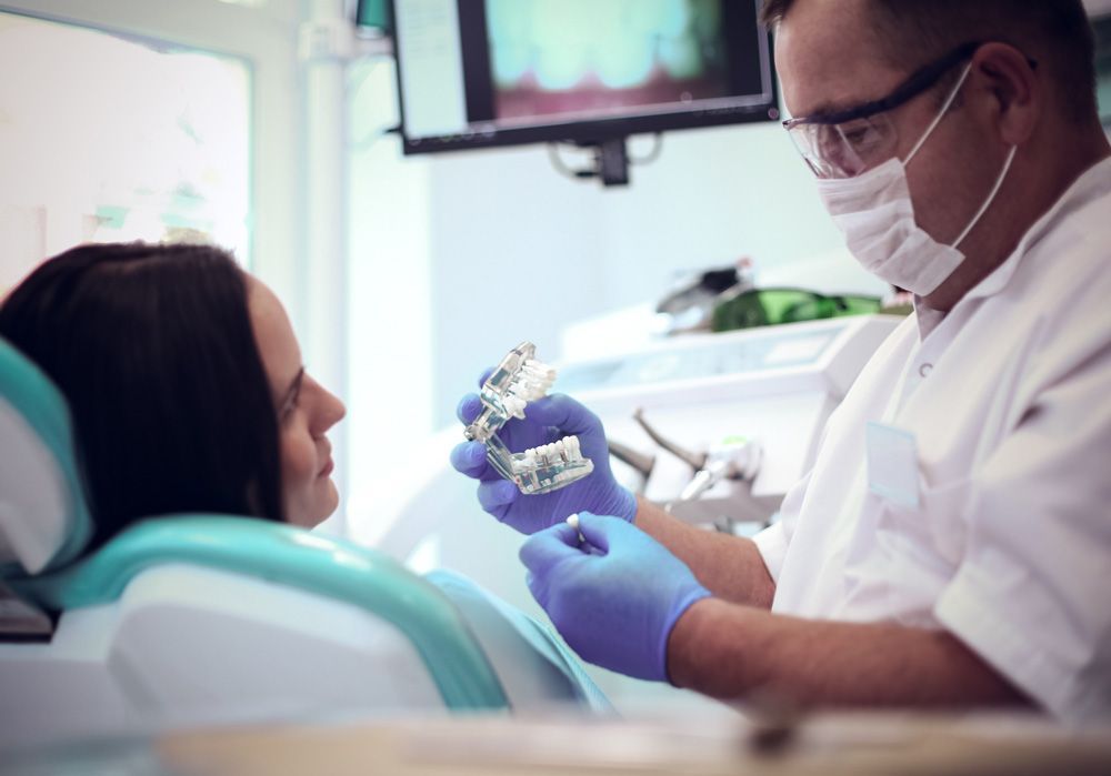 Una mujer está sentada en una silla dental mientras un dentista le examina los dientes.