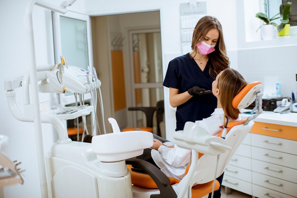 Una mujer está sentada en una silla dental hablando con un dentista.