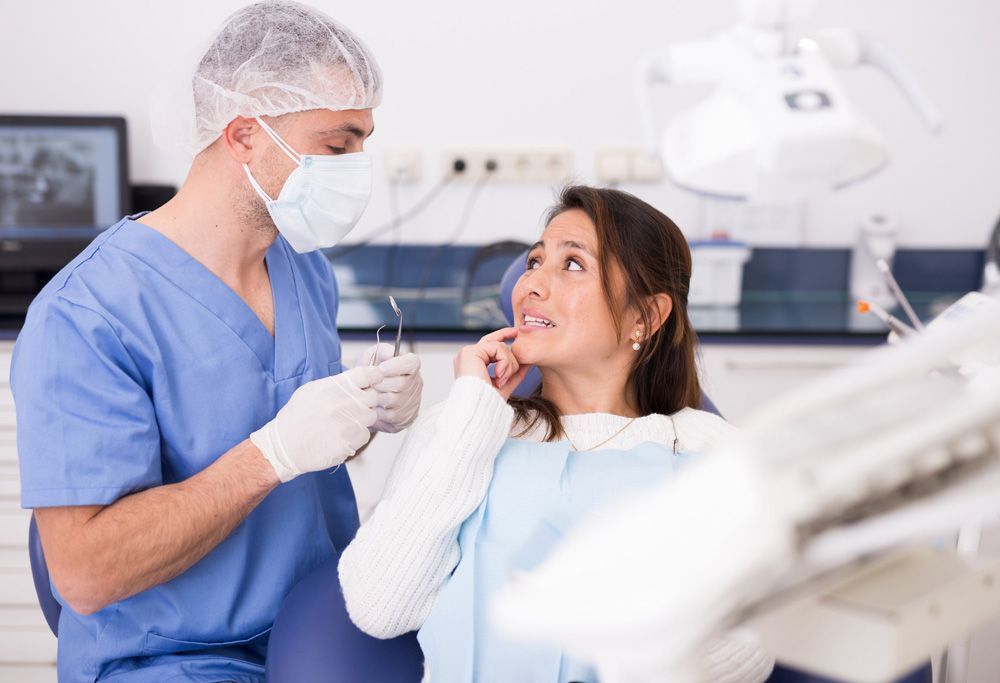 Una mujer está sentada en una silla dental mientras un dentista le examina los dientes.