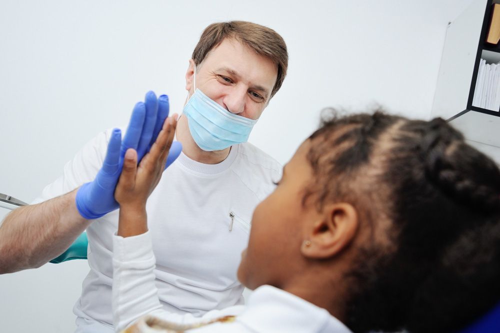 Un dentista le choca los cinco a un niño mientras usa una mascarilla y guantes.