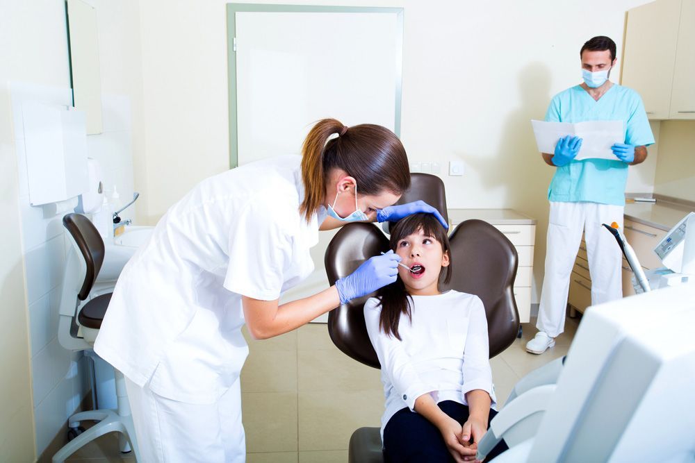 Una niña está sentada en una silla dental mientras un dentista le examina los dientes.