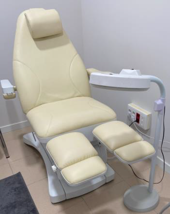 Sillón de spa color crema con reposapiernas, reposabrazos y reposacabezas ajustables, junto a una lámpara. En una sala de spa.