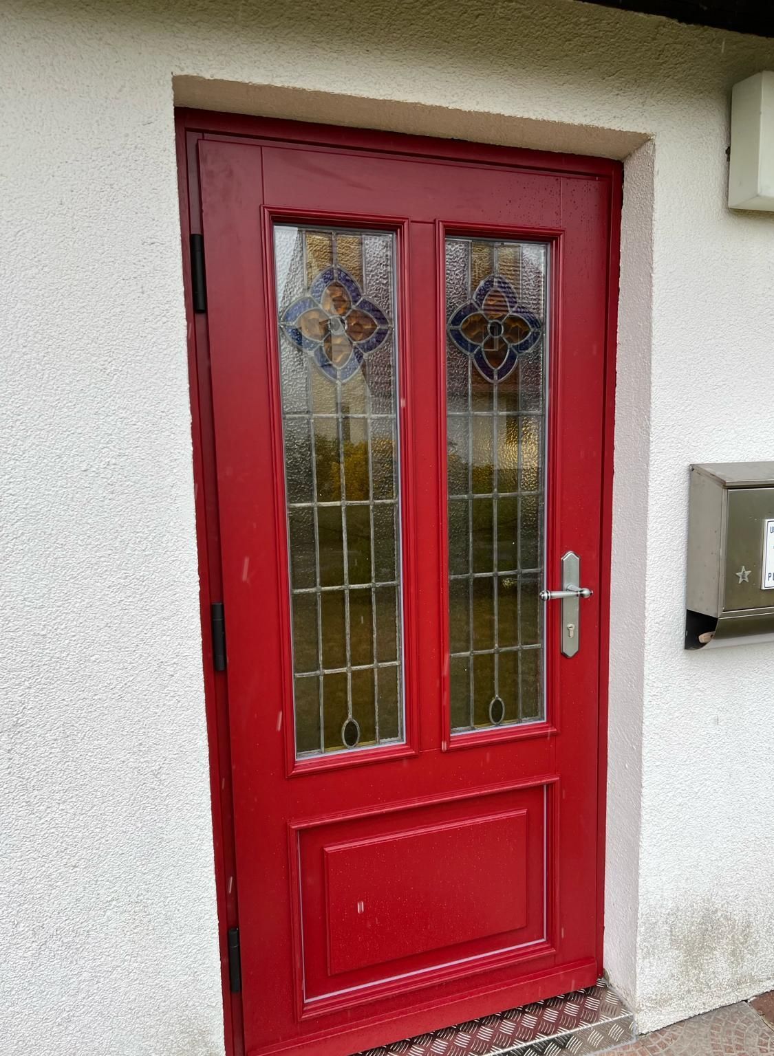 An einer weißen Wand befindet sich eine rote Tür mit Buntglasfenstern | Tischlermeister DANIEL NETZ