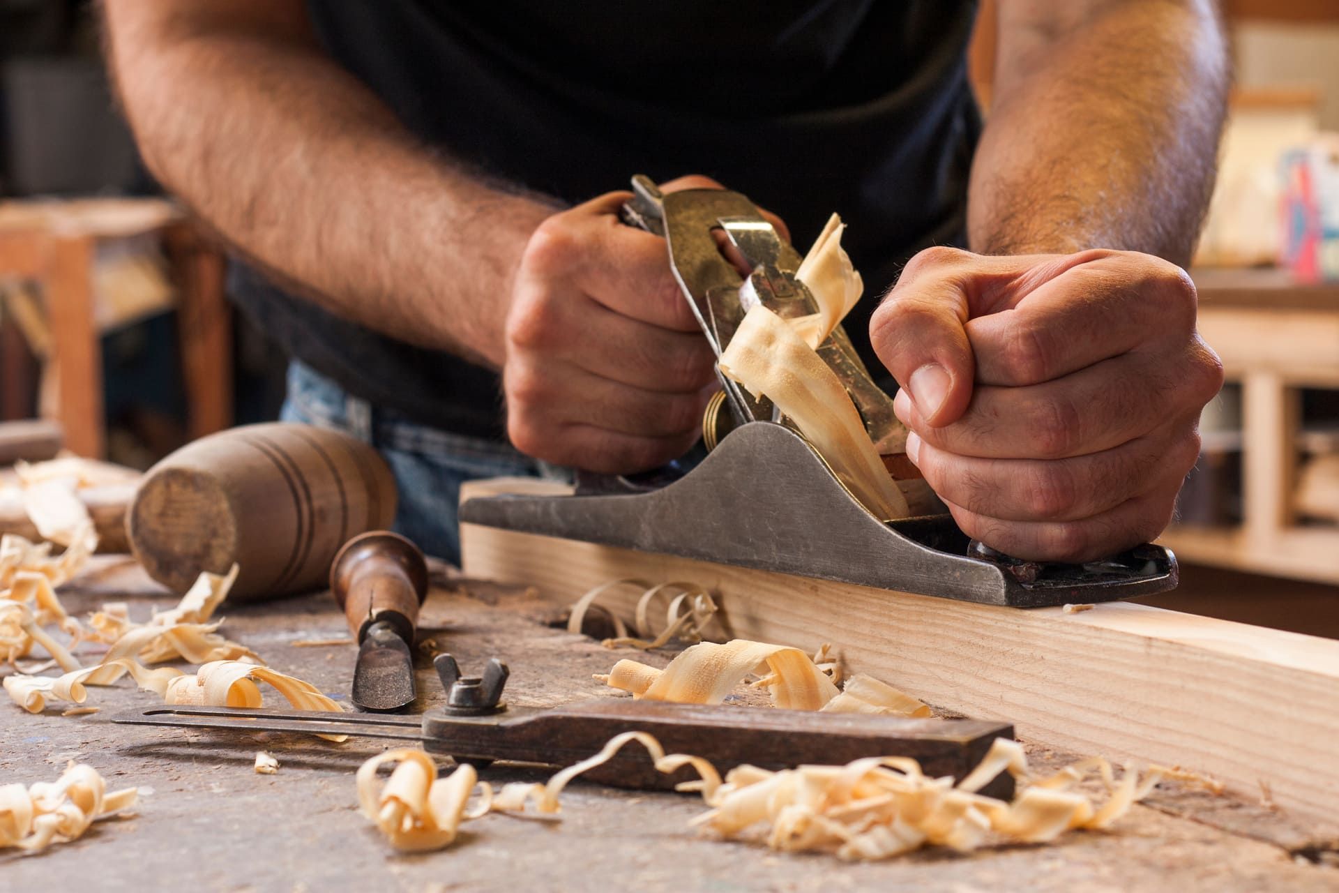 Ein Mann hobelt mit einem Hobel ein Stück Holz | Tischlermeister DANIEL NETZ