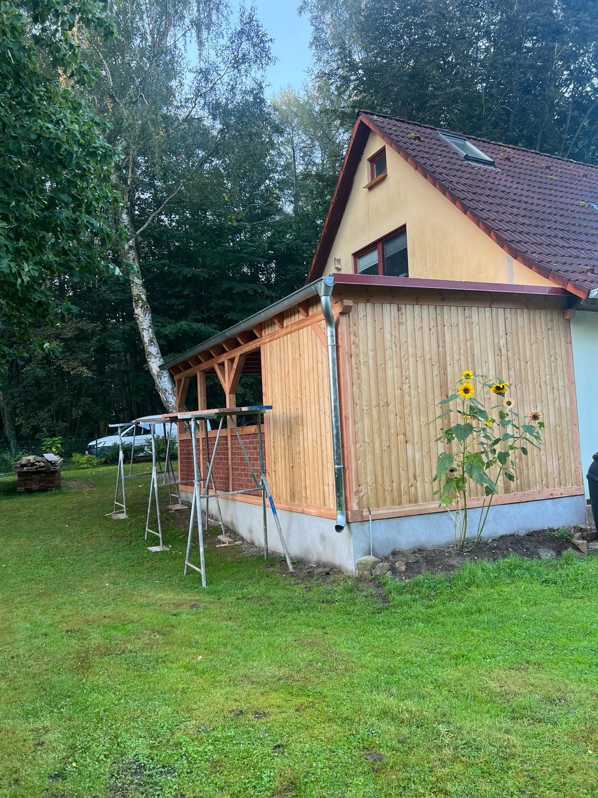 Ein Haus mit einer Holzveranda steht inmitten einer üppigen grünen Wiese | Tischlermeister DANIEL NETZ