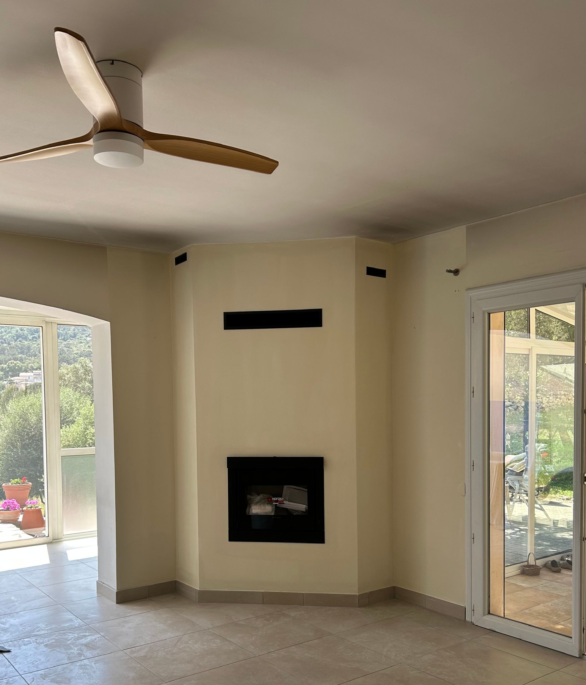 Salon vide avec ventilateur de plafond, cheminée et grandes portes coulissantes en verre des deux côtés