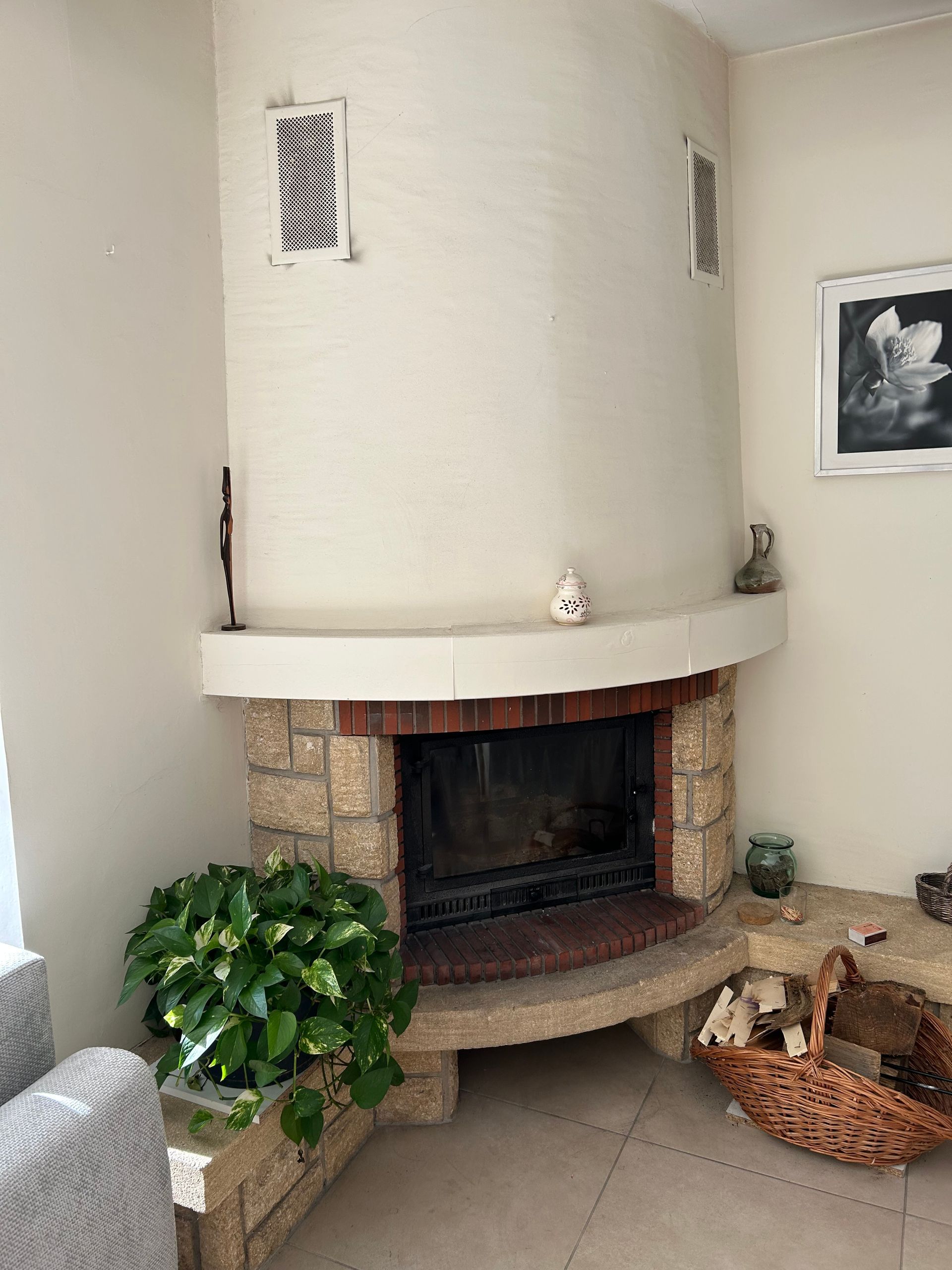 Cheminée d'angle avec conduit blanc, entourage en briques, plante et panier de bois de chauffage dans un salon