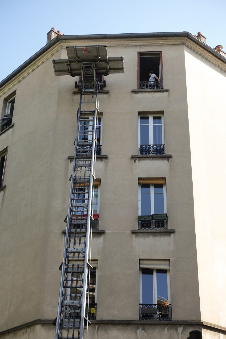 Un ascenseur extérieur dessert la fenêtre du dernier étage d'un immeuble beige à plusieurs étages en ville.