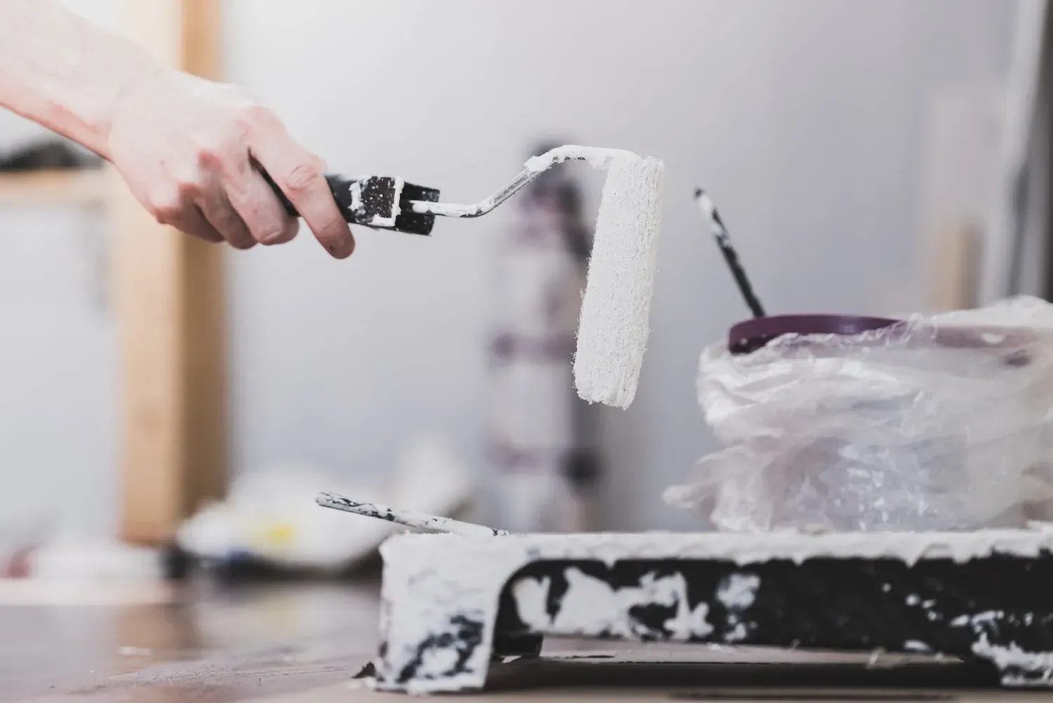 Una mano sostiene un rodillo de pintura blanco sobre una bandeja de pintura con un revestimiento de plástico.