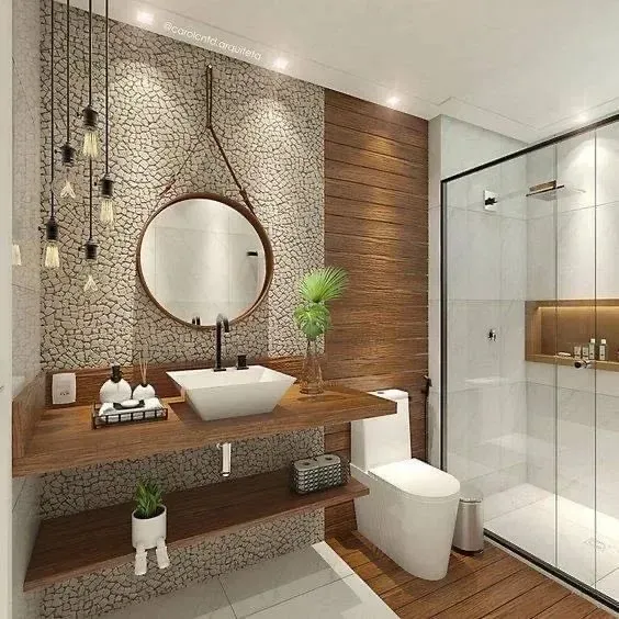 Baño moderno con una pared decorativa con textura de guijarros, un tocador flotante de madera, un espejo circular y una ducha de cristal.