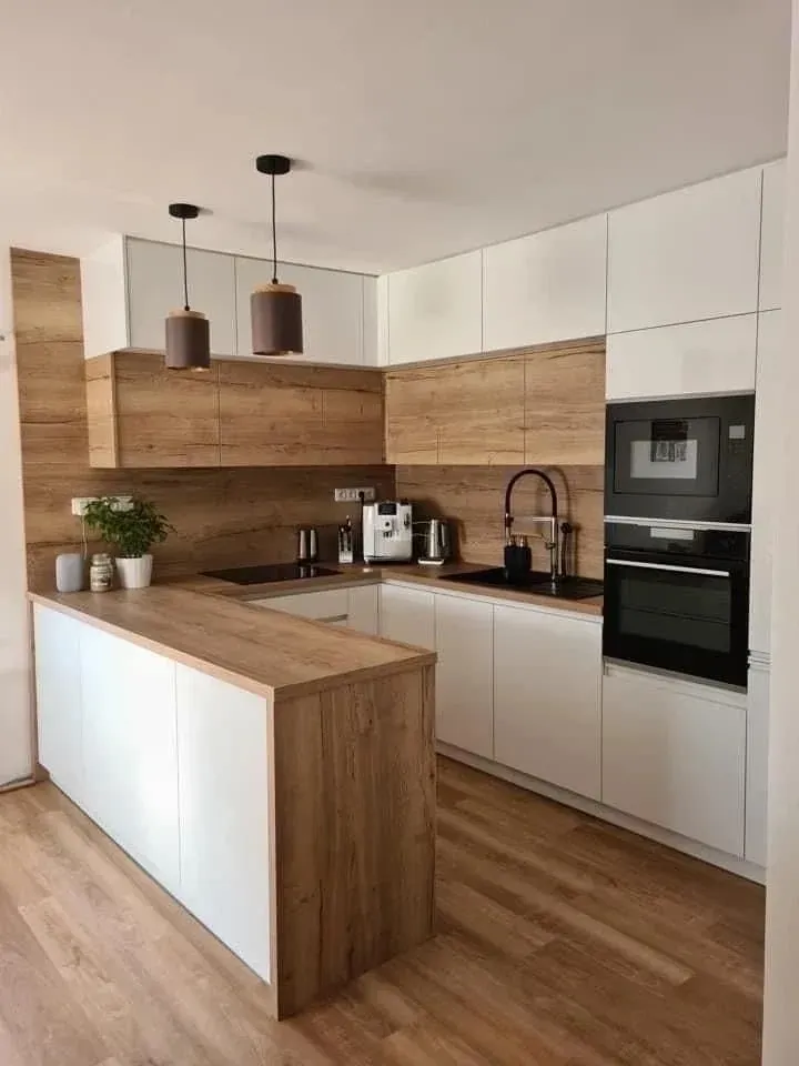 Una cocina moderna con gabinetes blancos, encimeras de madera clara, una barra de desayuno y electrodomésticos negros integrados.