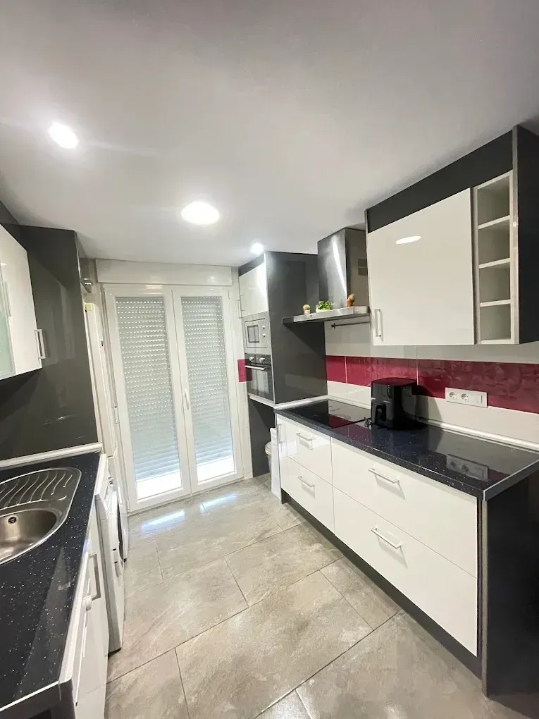 Una cocina moderna con gabinetes blancos con detalles en gris oscuro, una encimera oscura y un protector contra salpicaduras de azulejos rojos.