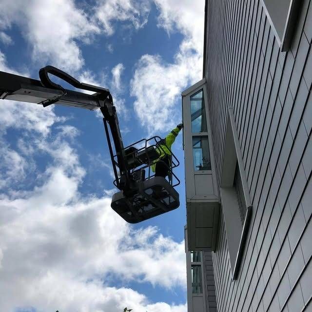 Fensterputzer arbeitet in einer Hubarbeitsbühne neben einem modernen Gebäude vor einem bewölkten Himmel