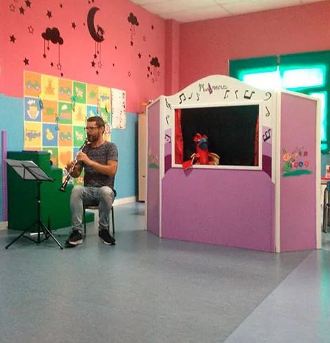 Un hombre tocando el clarinete frente a un teatro de marionetas.