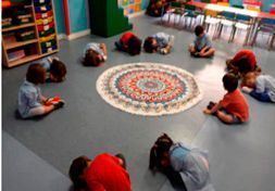 Un grupo de niños está sentado en círculo en el suelo en un aula.