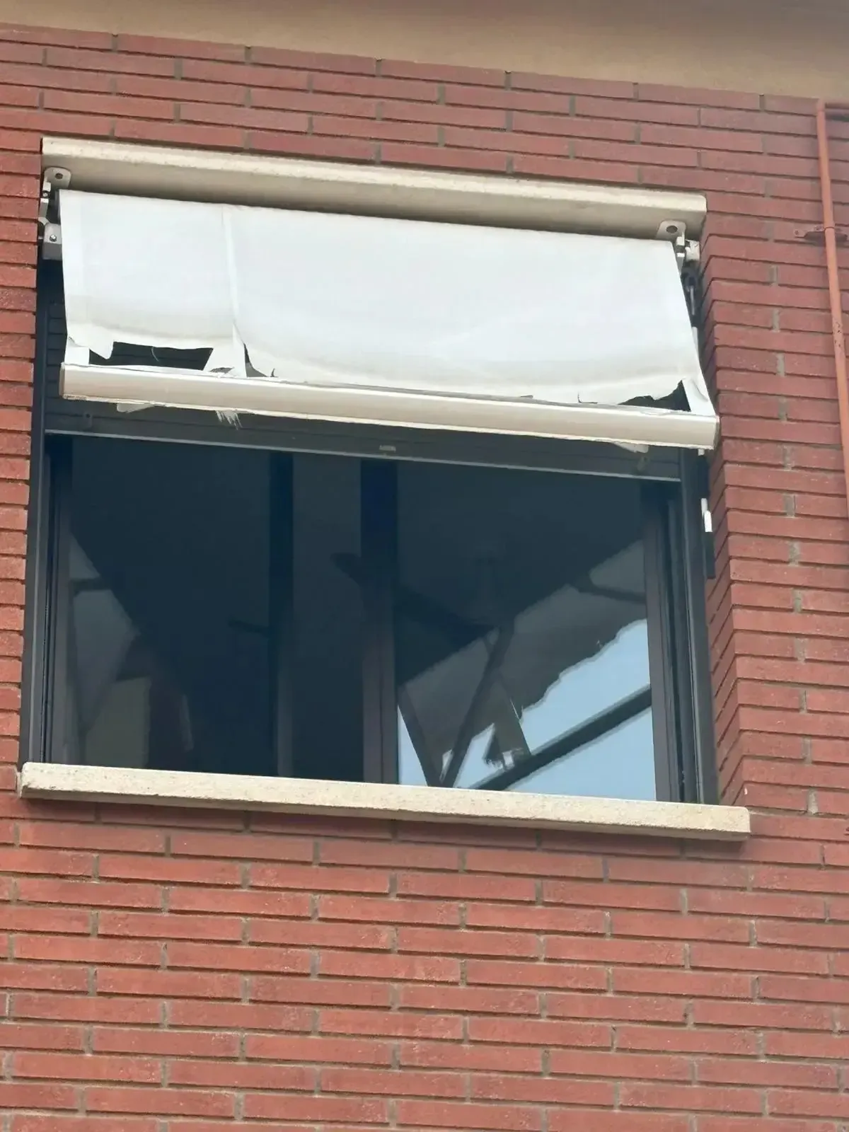 Ventana con un toldo blanco roto contra un edificio de ladrillo rojo.