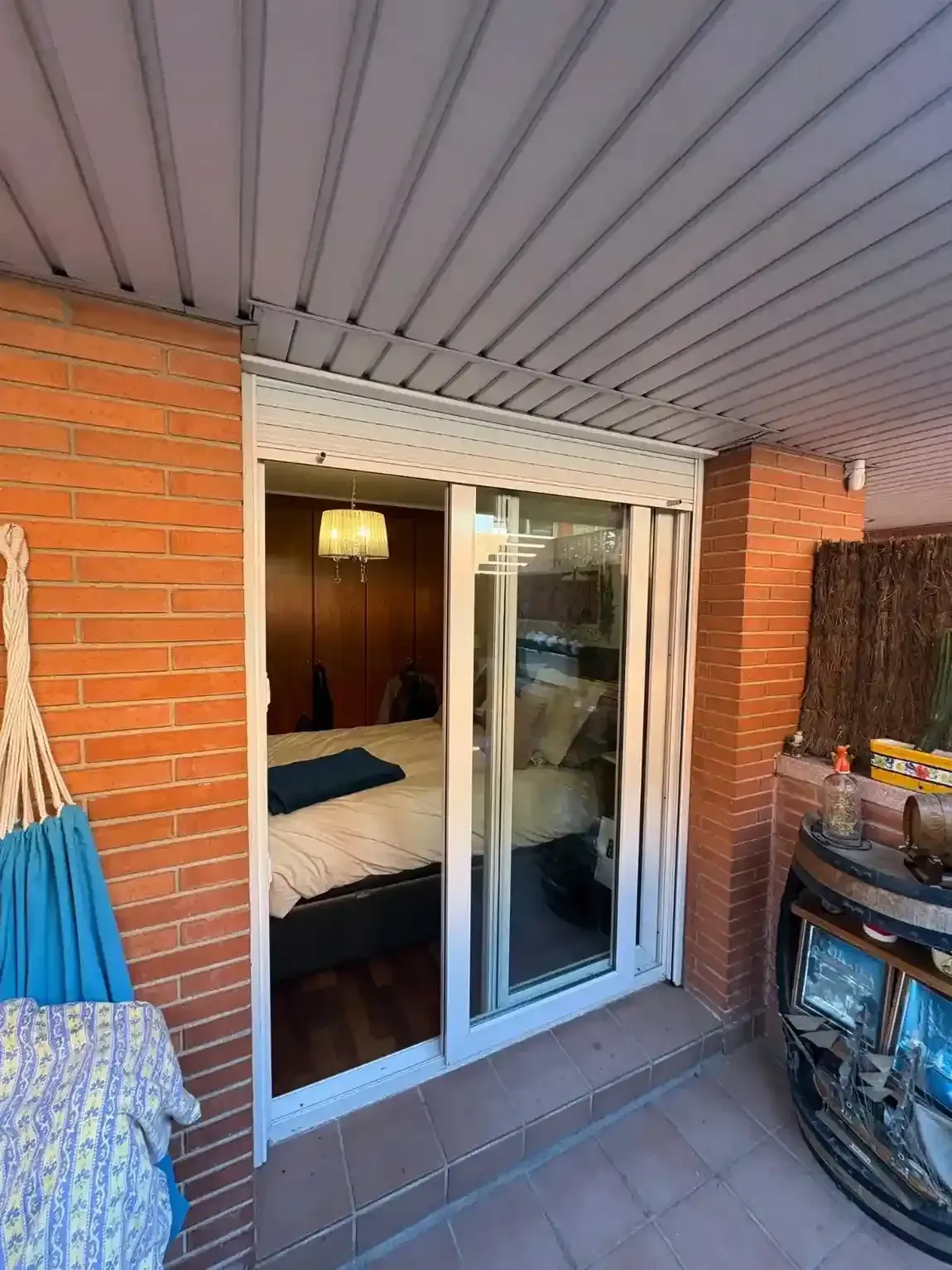 Patio con puerta corrediza de vidrio, paredes de ladrillo y vista a un dormitorio con cama.