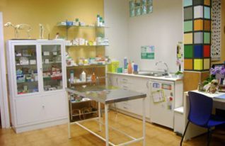 Sala de laboratorio con armarios, mostradores, equipos y una mesa central de acero inoxidable.