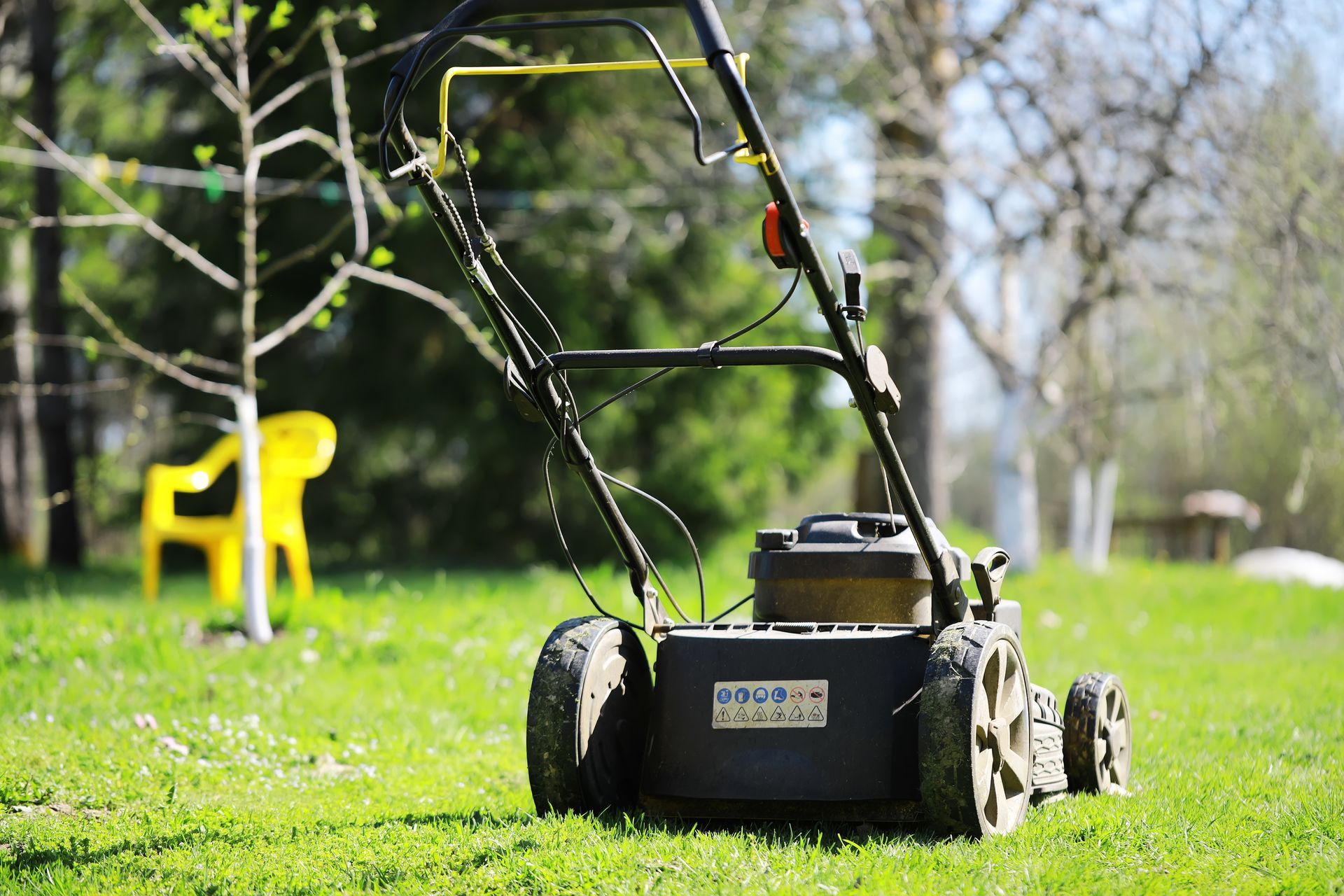 Tondeuse à gazon sur de l'herbe verte dans une cour ensoleillée, avec une chaise jaune en arrière-plan.