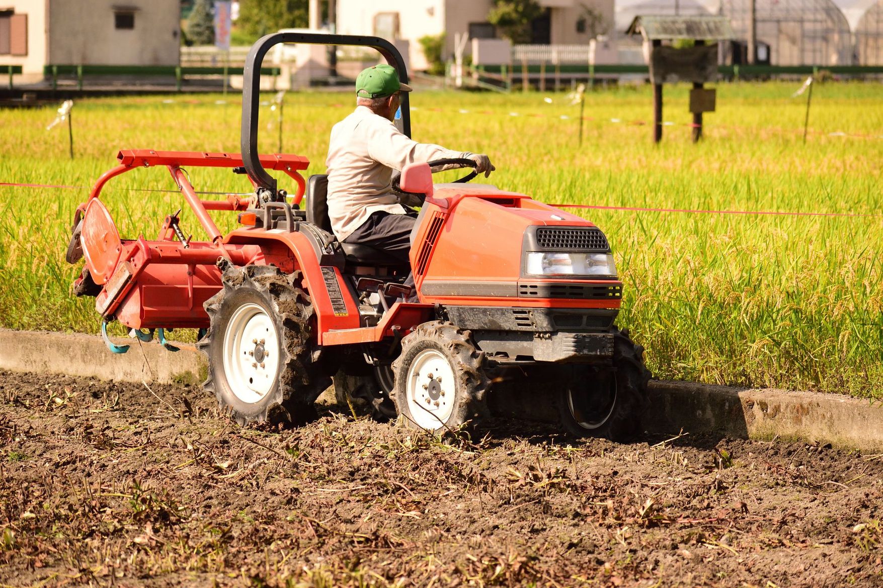Un agriculteur conduit un petit tracteur rouge dans un champ verdoyant et boueux.
