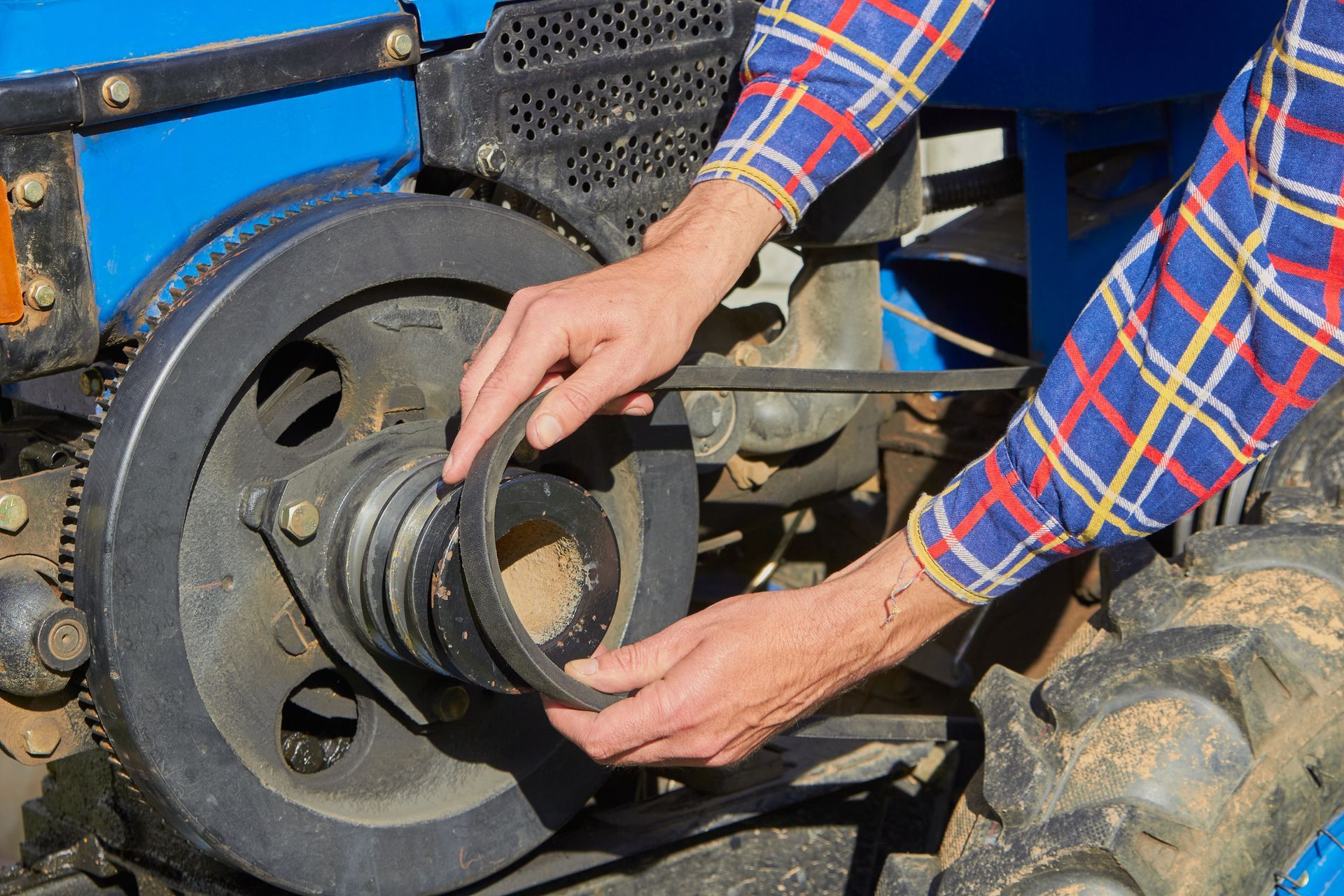 Gros plan de mains ajustant un accouplement mécanique noir sur un moteur de tracteur bleu