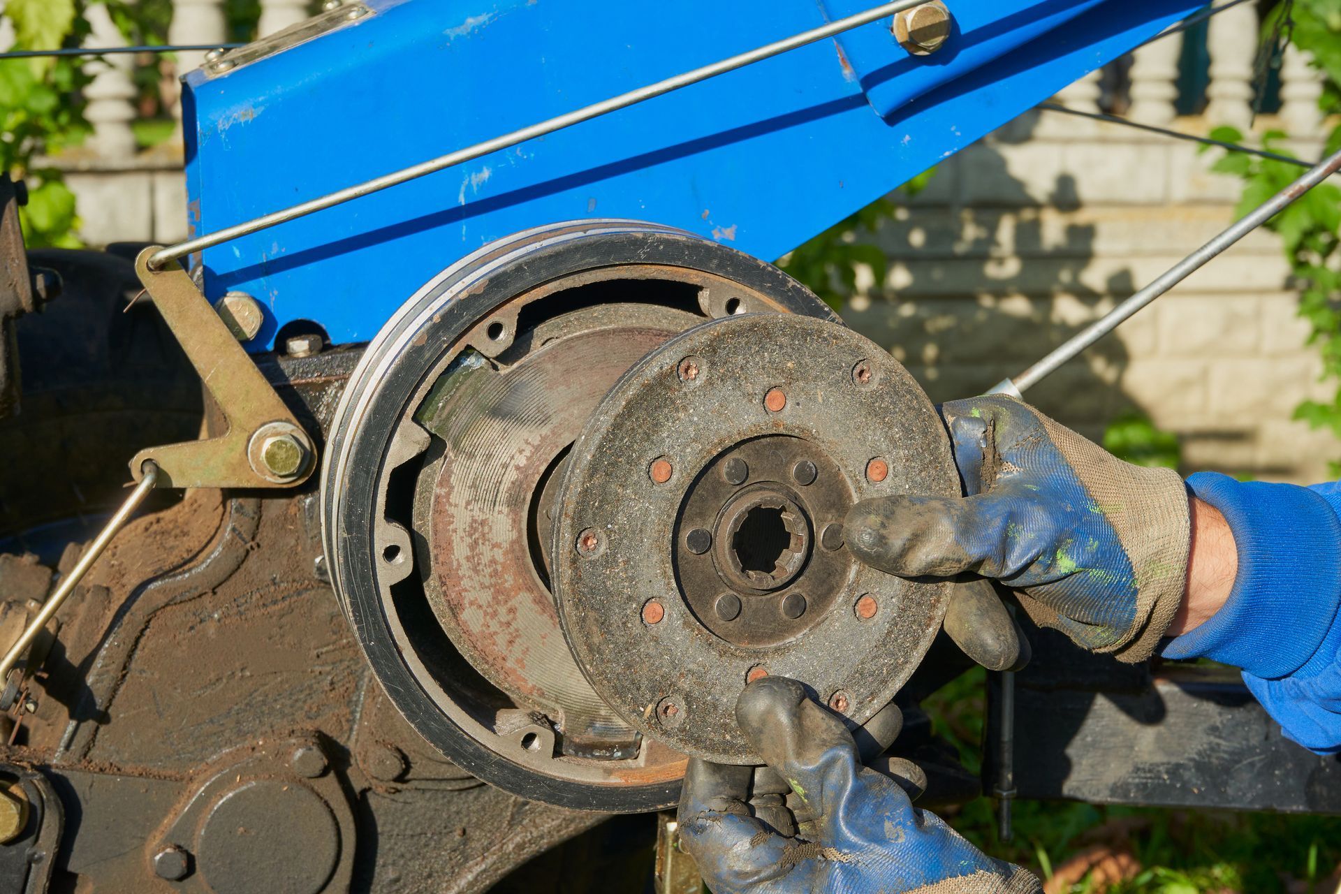 Des mains gantées retirent un tambour de frein rouillé d'un véhicule bleu à l'extérieur